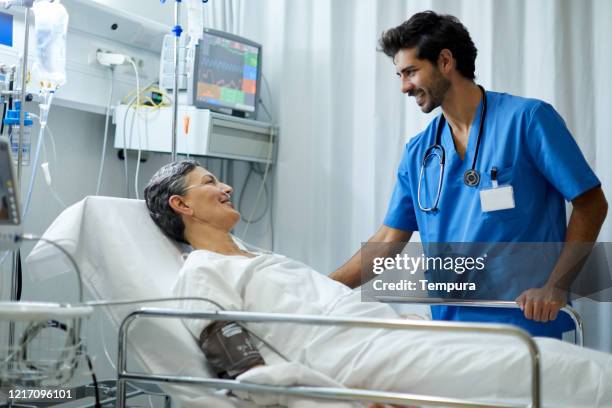 a male nurse is listening a patient in the recovery area. - adult male hospital bed stock pictures, royalty-free photos & images