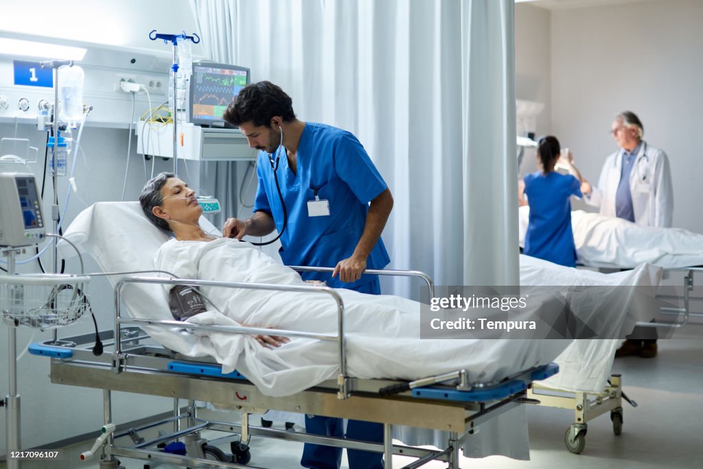 Eine männliche Krankenschwester hört mit einem Stethoskop das Herz eines Patienten.