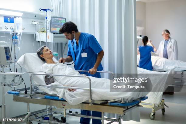 a male nurse is listening with a stethoscope the heart bit of a patient. - recovery room stock pictures, royalty-free photos & images