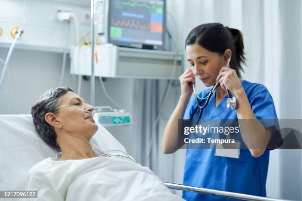 a nurse is putting the stethoscope on her ears to examine a patient. - post operation stock pictures, royalty-free photos & images