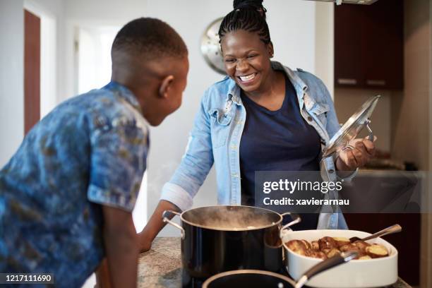 junger sohn beobachtet afrikanische mutter bereiten essen - black mother and child cooking stock-fotos und bilder