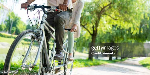 couple riding tandem bicycle in park - tandem stock pictures, royalty-free photos & images