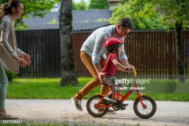 father teaching son to ride bicycle - father helping son wearing helmet stock pictures, royalty-free photos & images