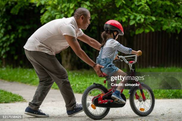 vater lehrt seine tochter, fahrrad zu fahren - bicycle daughter stock-fotos und bilder