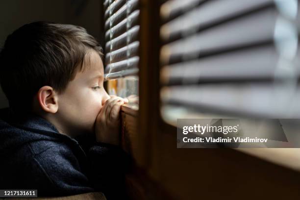 kleine droevige jongen die door het venster tijdens isolatie coronavirus kijkt. - protection stockfoto's en -beelden