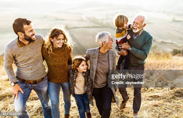 happy multi-generation family talking while taking a walk on the field. - multi generation family stock pictures, royalty-free photos & images