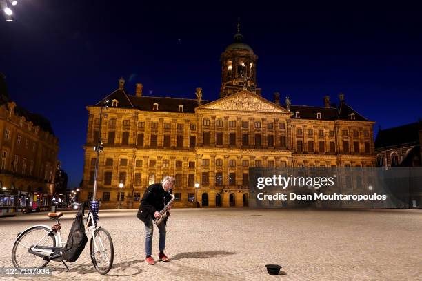 Busker plays in front of the Koninklijk Paleis or The Royal Palace Amsterdam , which is closed to the public until further notice on April 04, 2020...