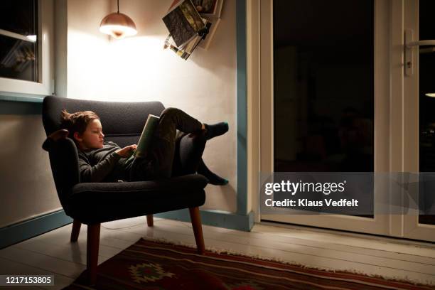 Boy reading book under lamp in armchair at night