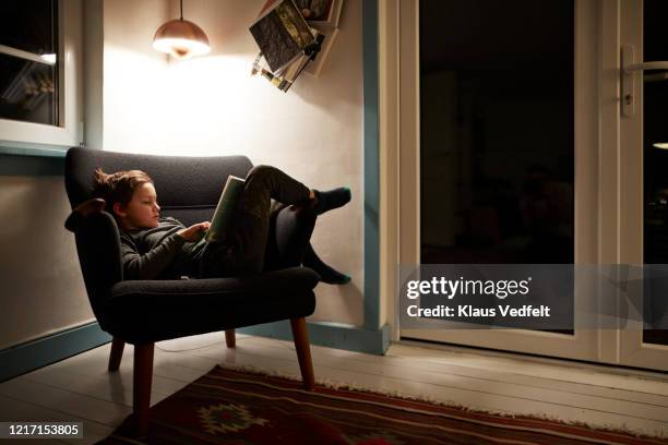 boy reading book under lamp in armchair at night - electric lamp 個照片及圖片檔
