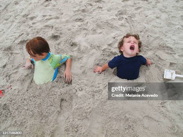 two little children buried in the sand at the beach with the ocean behind them. you can just see them from the chest up. - just buried stock pictures, royalty-free photos & images