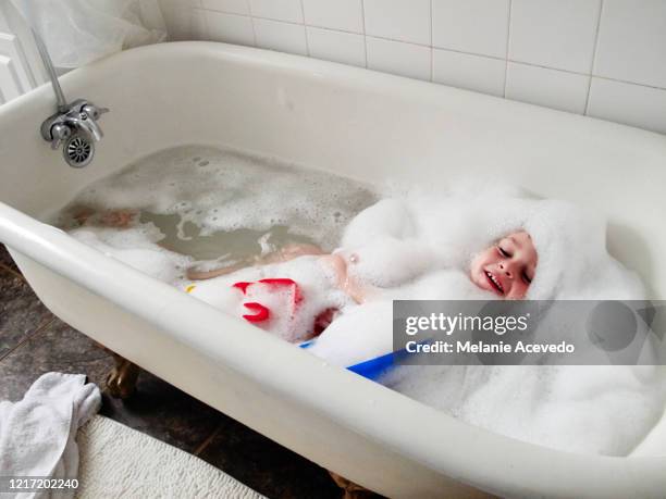 young boy with brown curly hair brown eyes playing in bath tub covered in bubbles - badewanne schaum stock-fotos und bilder