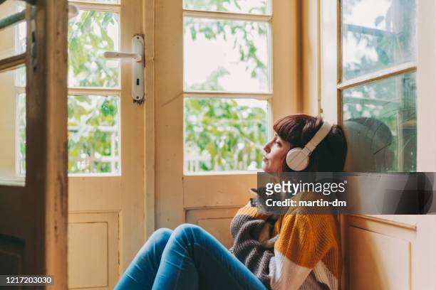 woman staying home due to covid-19 pandemic - listening imagens e fotografias de stock