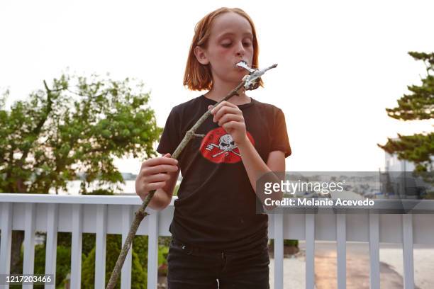 young redheaded girl short hair brown eyes freckles standing on porch eating marshmallow pulling piece off of stick looking down at burnt marshmallow on stick - child pulling hair stock pictures, royalty-free photos & images
