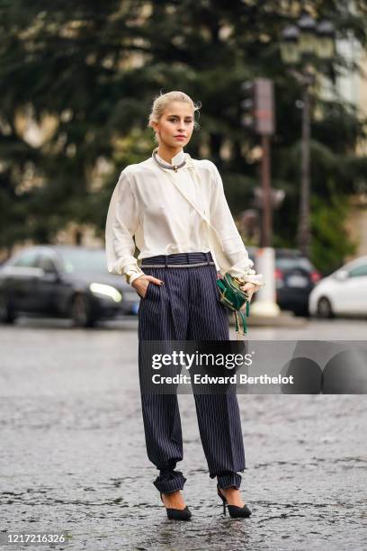 Caroline Daur wears a necklace, a white flowing shirt, navy blue striped pants, a green leather crocodile pattern Chloe bag, a belt, black high heels...