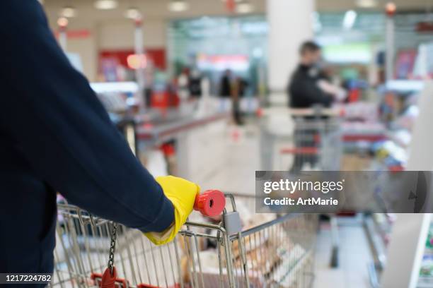 hombre con guantes de goma y sosteniendo el carro de la compra en una línea con distancia social - hacer cola fotografías e imágenes de stock