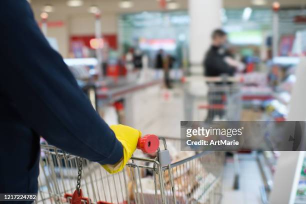 man wearing rubber gloves and holding shopping cart in a line with social distancing - social distancing shopping stock pictures, royalty-free photos & images