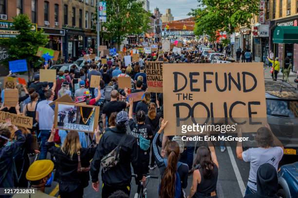 Participant holding a Defund The Police sign at the protest. Thousands of protesters filled the streets of Brooklyn in a massive march to demand...