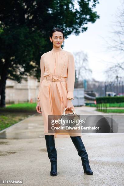 Ai Tominaga wears a pale pink flowing dress, golden bracelets, a white Chloe bag, black leather long boots, outside Chloe, during Paris Fashion Week...