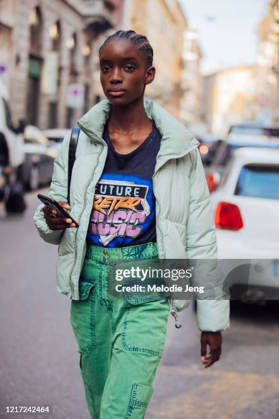 Model Maty Fall wears a green puffer jacket, blue Future Retro Music t-shirt, green acid wash pants, and checks her iPhone 11 after the Ports 1961...