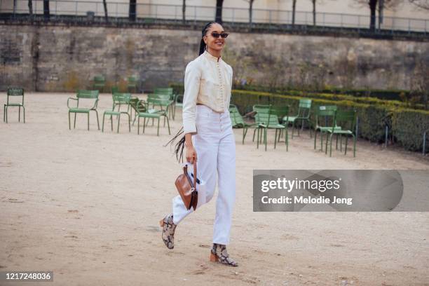 Model Indira Scott wears a cat-eye sunglasses, vintage-style cream button-up top , white jeans, a small brown bag, and python boots after the Dior...