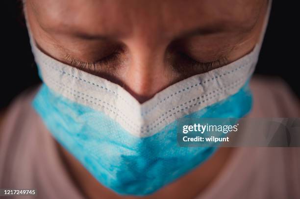 surgical mask portrait of a sad woman looking down with running tear - ebola stock pictures, royalty-free photos & images