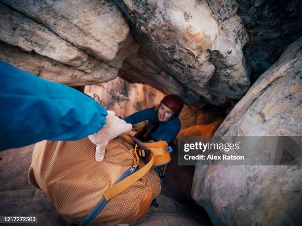 point of view passing a backpack down into cave like tunnel to a women - spelunking stock-fotos und bilder