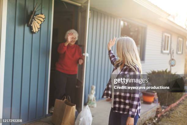 mature adult female delivering groceries to senior adult female and social distancing due to infectious virus outbreak pandemic - waving goodbye stock pictures, royalty-free photos & images