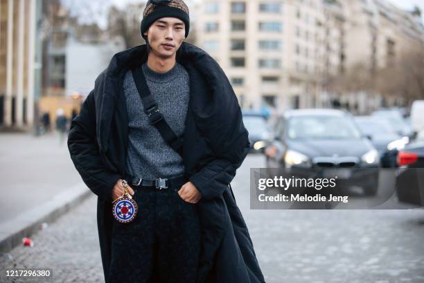 Model Tae Min Park wears a black and gold beanie, black coat, gray sweater, small circular accessory, Dior bag, Alyx belt, and black moon-print pants...