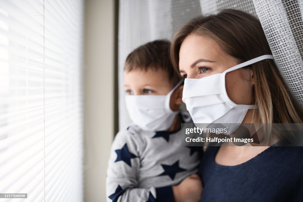 Mother and small son with face mask indoors at home, quarantine concept.