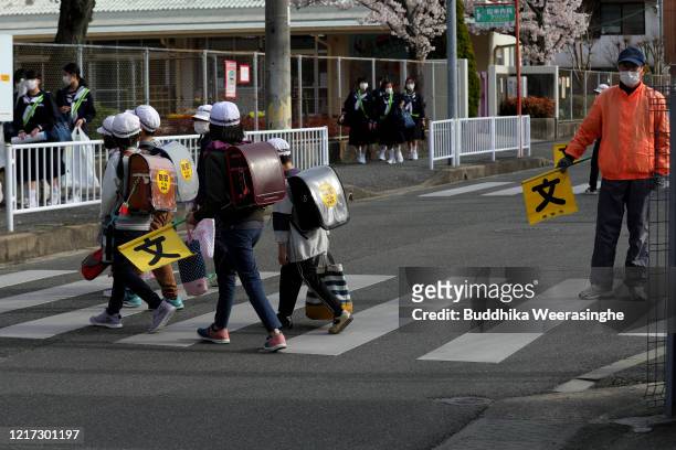 Students wear face masks cross the road on April 7, 2020 in Himeji, Japan. Nationwide most of the school resumed its new academic year today for...