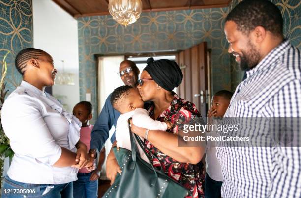 grandmother kissing granddaughter hello as grandparent arrive to visit family - black family reunion stock pictures, royalty-free photos & images