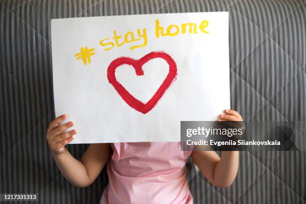 close up of child's hands holding a piece of paper with text stay home and red heart. - baby background stockfoto's en -beelden