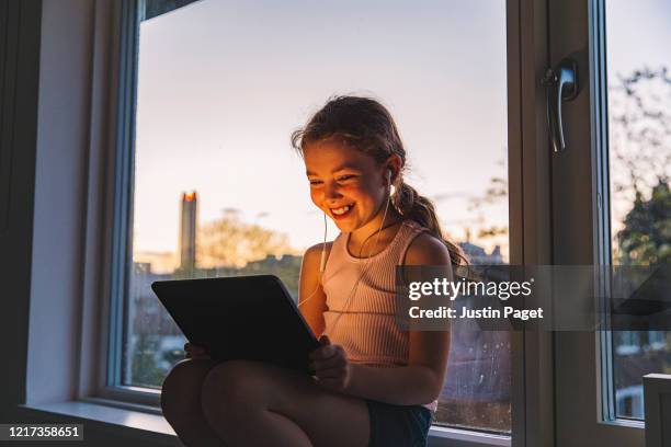 young girl using digital tablet by window - children on a tablet stockfoto's en -beelden