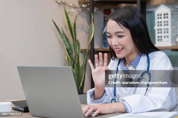 an asian doctor waves while video chatting with colleague. - stralende lach stockfoto's en -beelden