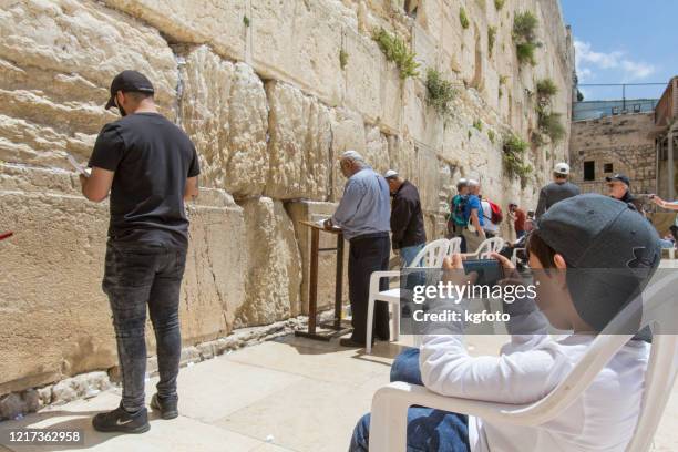 jews praying at western wall, wailing wall, kotel in old city of jerusalem, israel and a young jewish boy playing with his mobile phone waiting his father - yarmulke stock pictures, royalty-free photos & images