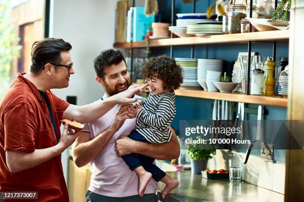 male parents playing with young son in kitchen - young gay couple stock pictures, royalty-free photos & images