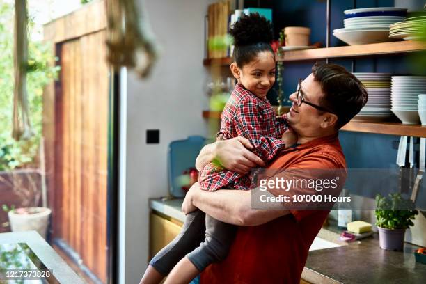 man holding adopted daughter in kitchen - person gemischter abstammung stock-fotos und bilder