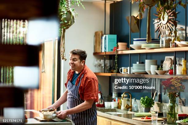 cheerful man preparing homemade in kitchen - stereotypical foto e immagini stock