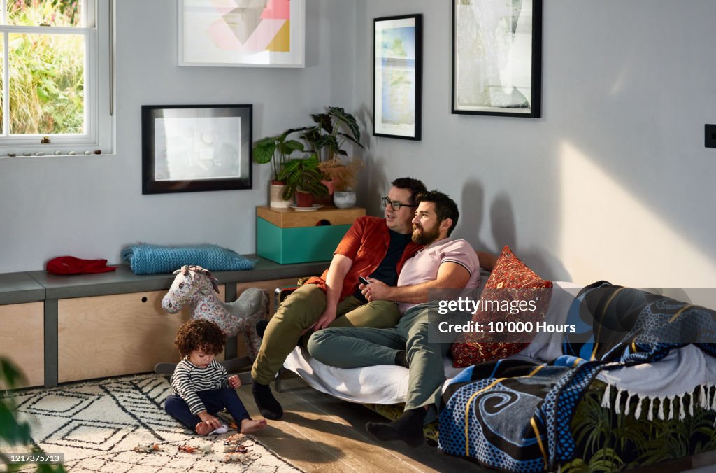 Gay couple watching television with son playing on floor