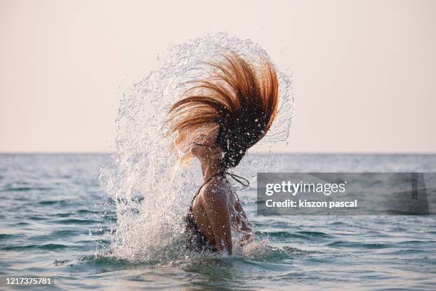 asian woman doing a water spin with her hair in the ocean during sunset . - woman twirling stockfoto's en -beelden