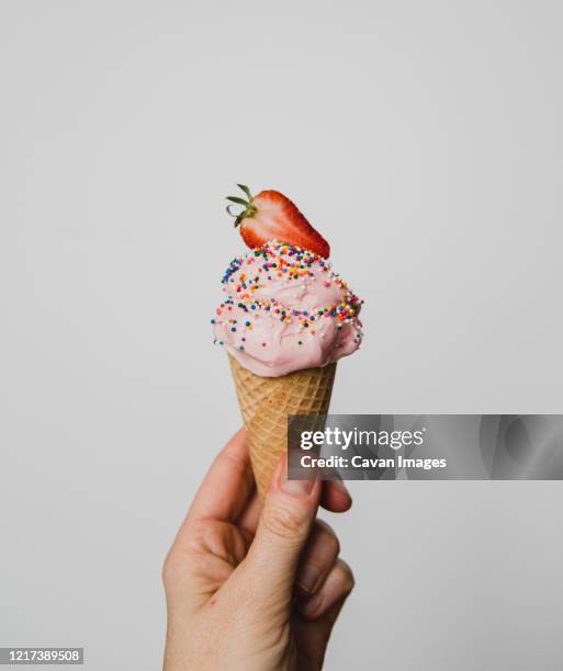 hand holding strawberry ice cream cone against white background. - softeis stock-fotos und bilder