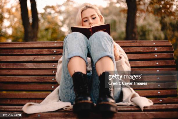 teenage girl reading book while sitting on bench in park during autumn - autumn kyiv stock pictures, royalty-free photos & images