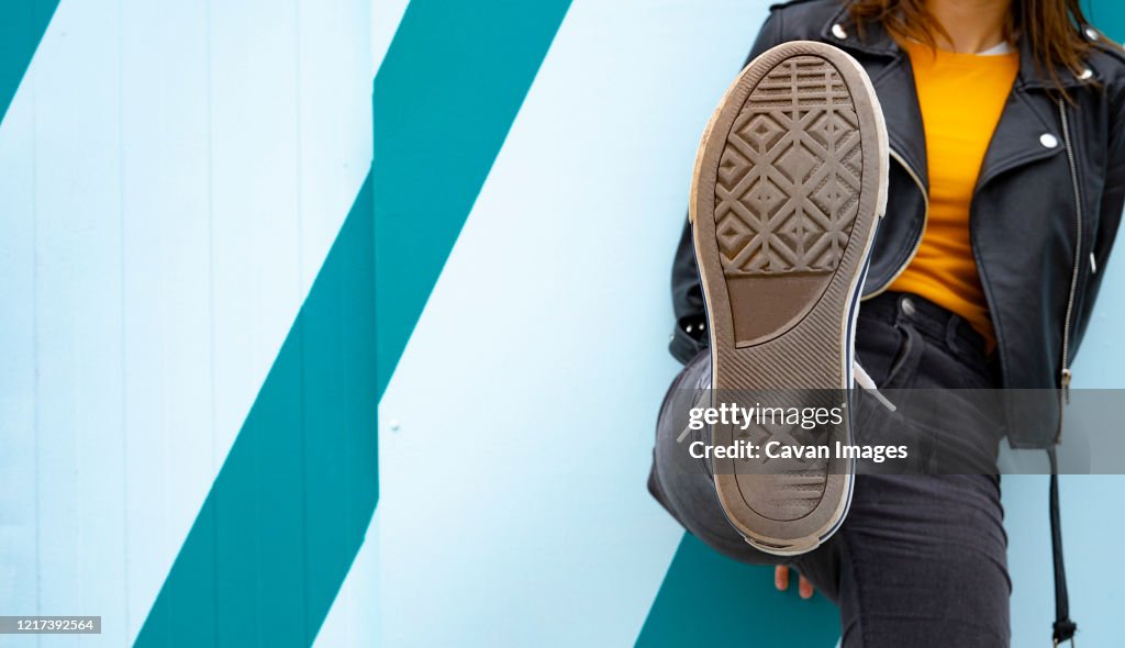 Woman showing the sole of her sneaker on a blue background.