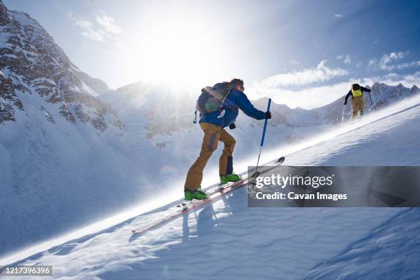 man ski touring up hill in the wind and backlit by the sun - skischoen stockfoto's en -beelden