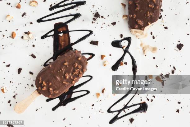chocolate ice cream bars on white with chocolate drizzle and nuts - belostomatidae stock pictures, royalty-free photos & images