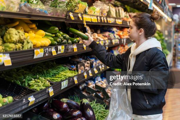 práctica de compras segura durante un brote de pandemia viral. una joven con guantes comprando verduras en una tienda. - panic buying fotografías e imágenes de stock