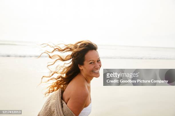 mujer madura riendo caminando en una playa en una tarde ventosa - cabello castaño fotografías e imágenes de stock