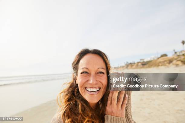 貝殻で海を聞く笑う成熟した女性 - beach shells ストックフォトと画像