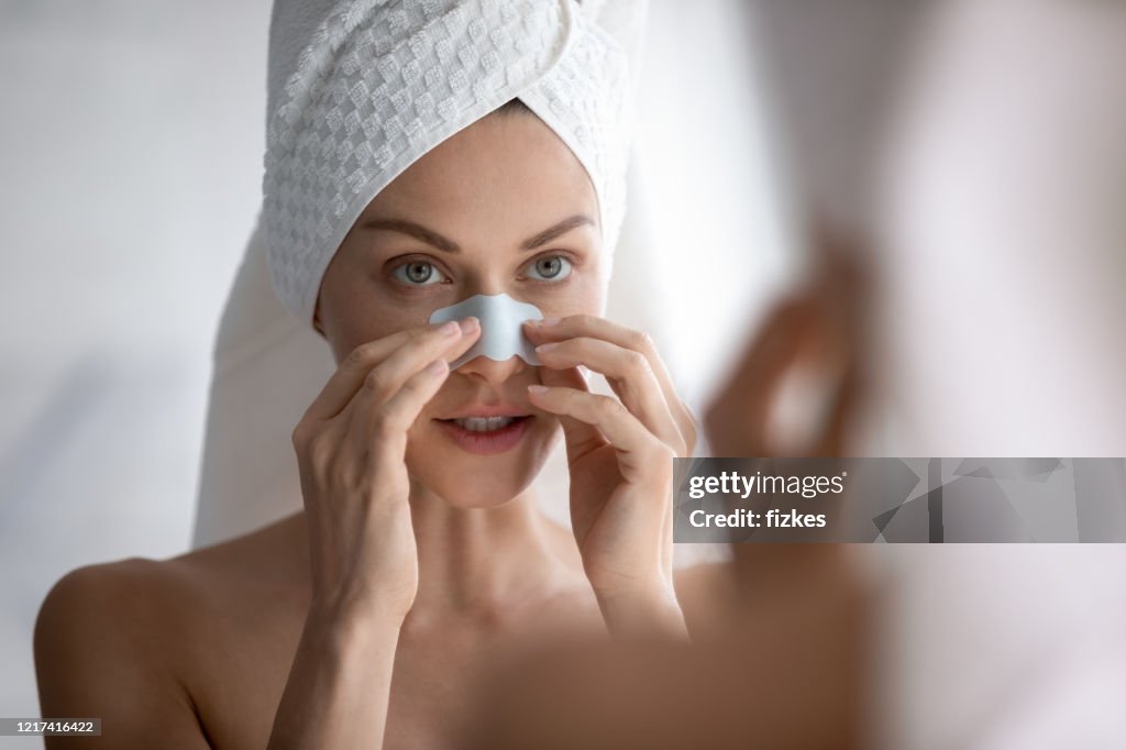 Young beautiful woman applying cleaning strip, removing dark spots.