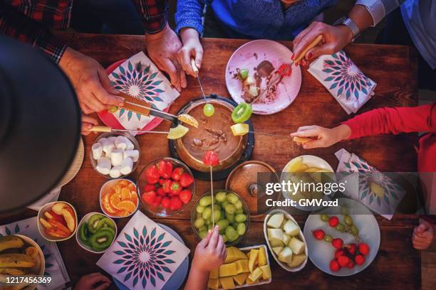 young family having delicious chocolate fondue in a pot served with fruits - chocolate fondue stock pictures, royalty-free photos & images